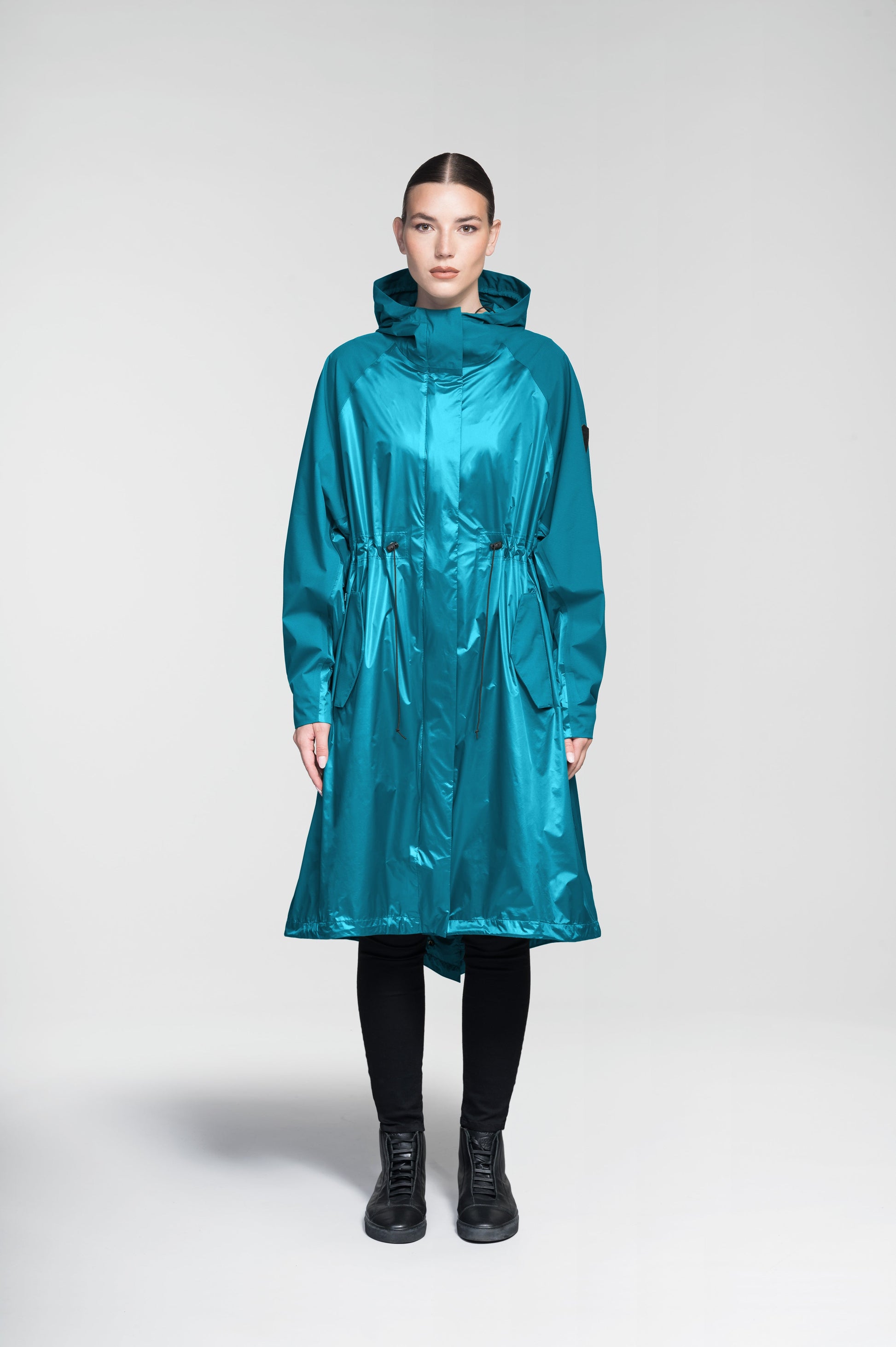 Reyna Women's Tailored Packable Long Shell Jacket in knee length, premium strech ripstop and contrast cire technical nylon taffeta fabrication, non-removable hood with adjustable draw cord, waist flap pockets with magnetic closures, adjustable draw cords at waist and bottom hem, adjustable snap cuffs, mesh back ventilation, hidden packable pocket, snap button wind flap, two-way branded zipper at centre front, adjustable snap button fishtail yoke at back, and large interior zipper pocket, in Deep Lake
