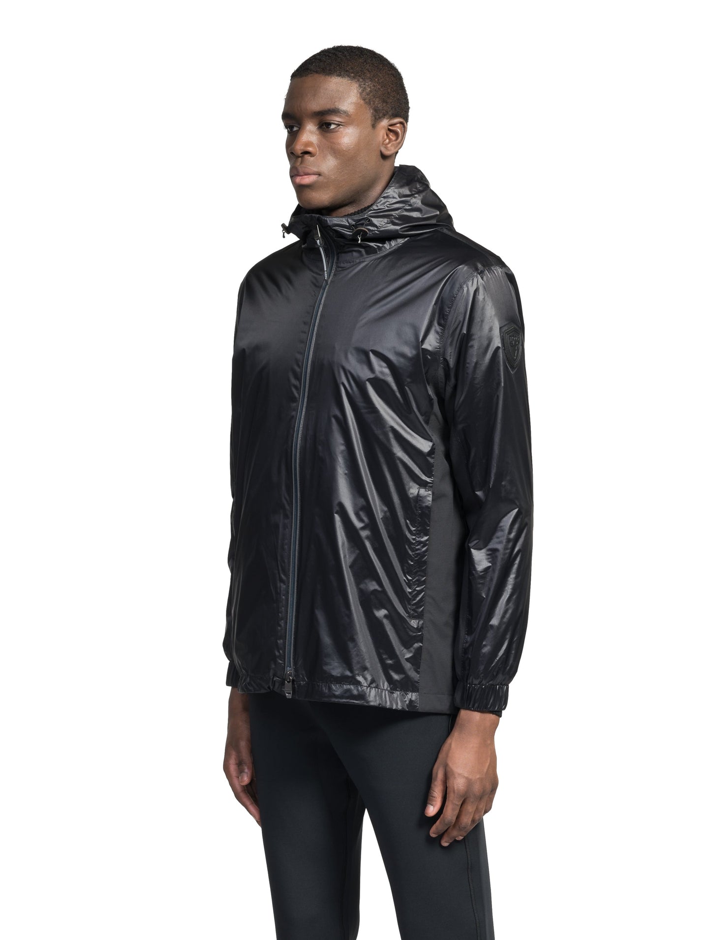 Stratus Men's Tailored Packable Rain Jacket in hip length, premium cire technical nylon taffeta and stretch ripstop fabrication, highly breathable mesh lining, hidden packable pocket, non-removable hood with adjustable draw cord, reflective piping along front and back, underarm grommets for extra breathability, back yoke with mesh ventilation, two waist zipper pockets, two interior zipper pockets, elastic cuffs with adjustable snap button, and adjustable interior draw cord at waist hem, in Black